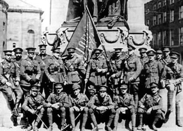 A group of British army officers pose beneath the statue of Parnell with the ‘Irish Republic’ flag that had flown over the GPO in O’Connell Street during the Easter Rising in 1916