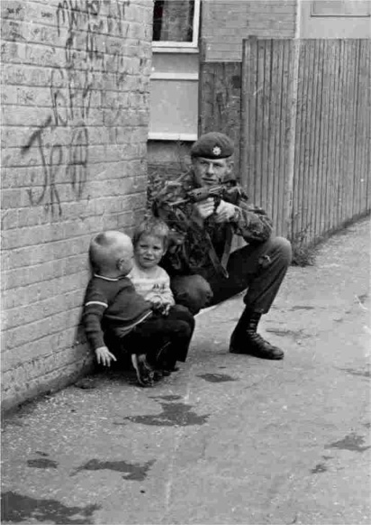 A British soldier on foot patrol in Belfast, Ireland, using two young Irish boys for cover